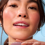 A person holds Tower 28 Beauty’s GetSet Powder Blush in the shade Samo Spritzer with a swatch of rosy mauve on their cheek. [Samo Spritzer]