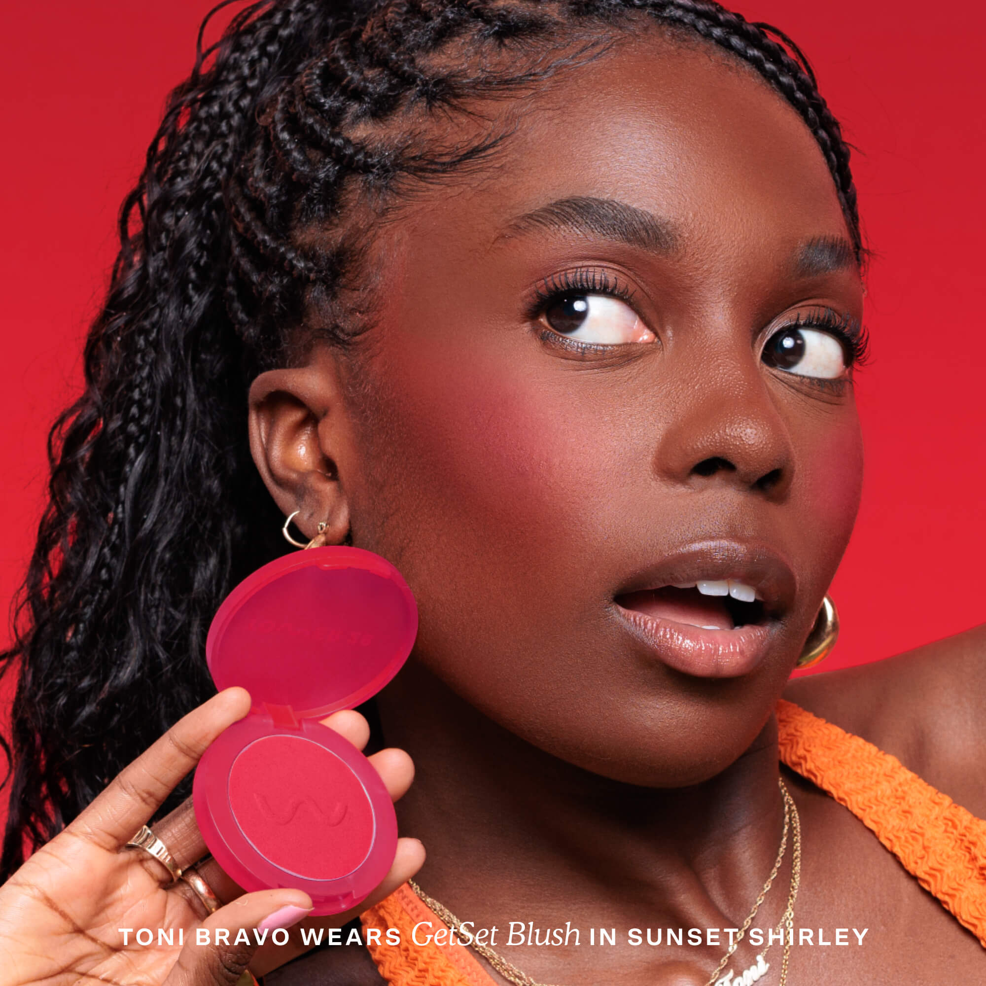Woman holding a pink makeup compact with a red background [Sunset Shirley x Toni Bravo]